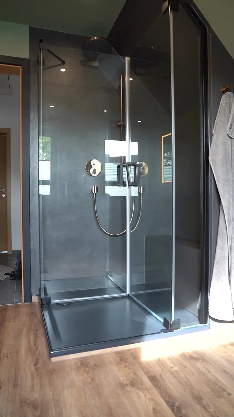 Dachgeschoss-Bad in Buxtehude: dunkle fugenlose Duschwand mit Armaturen in Bronze hinter Glas