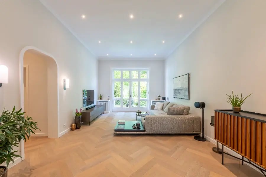 Altbausanierung Hamburg-Rotherbaum: Wohnzimmer nachher – heller Raum mit Rundbogen, Fischgrätparkett, großen Fenstern und Spots.