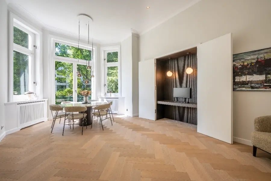 Altbausanierung Hamburg-Rotherbaum: Nachher – Erker mit Tageslicht, weiße Wände, Fischgrätparkett, integrierte Essbereich-Nische.