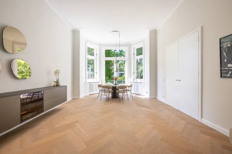 Altbausanierung Hamburg-Rotherbaum: Nachher-Foto – lichtdurchfluteter Erker, weiße Wände, Fischgrätparkett, moderner Essbereich.