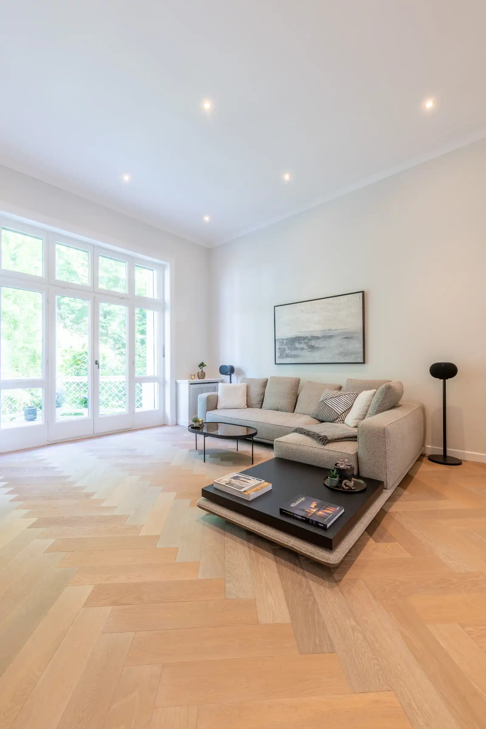 Altbausanierung Hamburg-Rotherbaum: Wohnzimmer nachher – große Fensterfront, helle Wände, modernes Sofa, Fischgrätparkett.