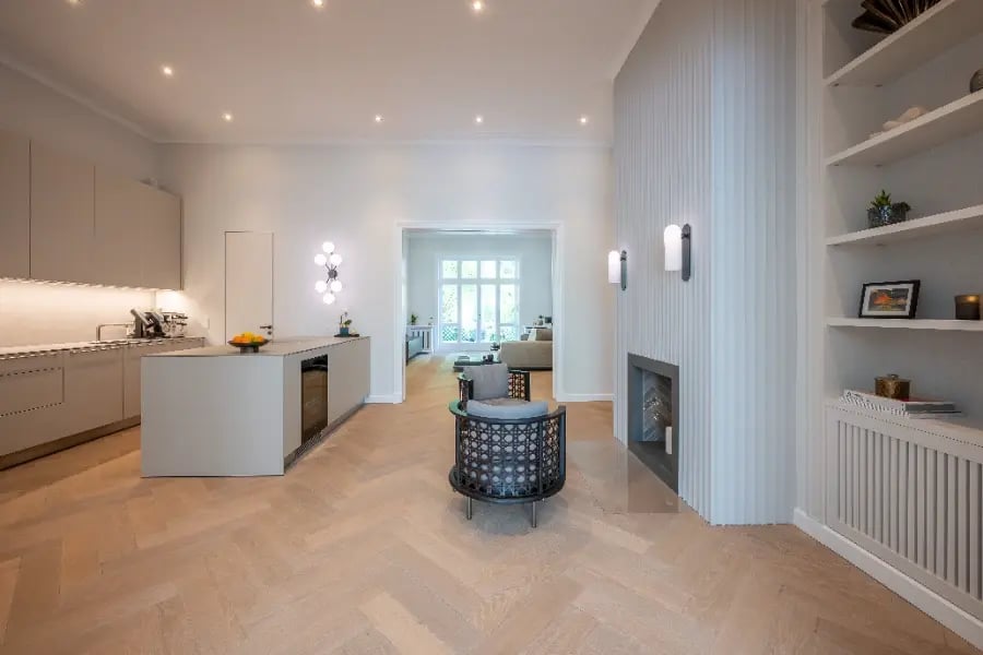 Altbausanierung Hamburg-Rotherbaum: Offene Küche mit Insel, Kaminwand, Einbauten und Eichen-Fischgrät; Blick ins Wohnzimmer.