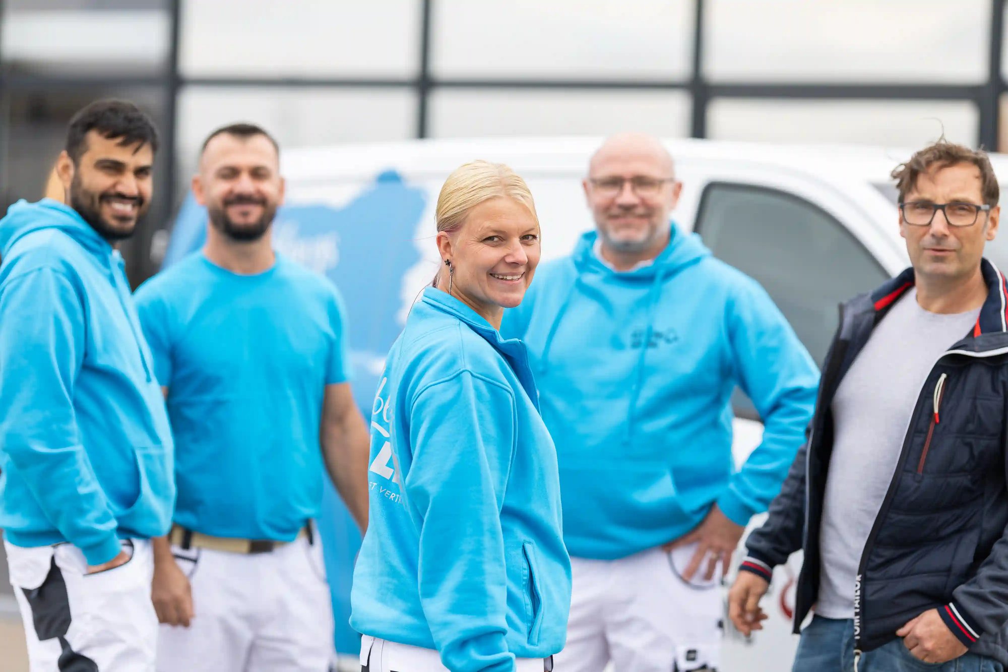 Fünf Teammitglieder von KS Farbkonzepte stehen vor einem gebrandeten Service-Van; die Kollegin in türkis lächelt in die Kamera – authentisches Teamfoto.
