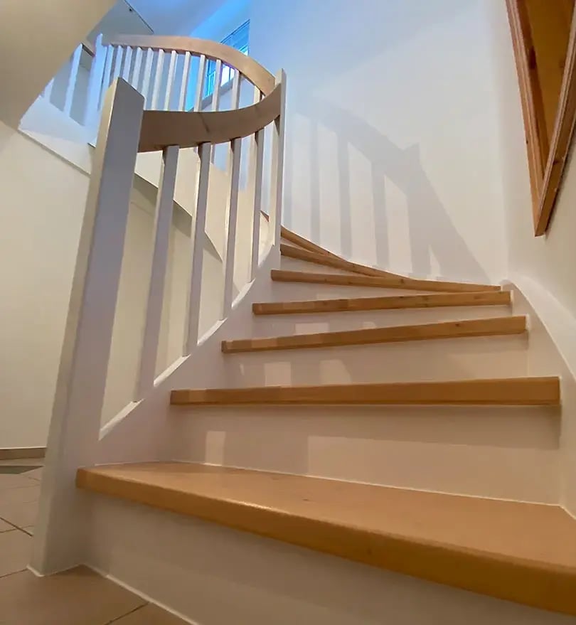 Das Ergebnis der Trerppenrenovierung: Wangen und Geländer in frischem Weiß lackiert, Trittstufen und Handlauf als wamer Holzkontrast erhalten. Der Flur wirkt sofort größer, heller und moderner.