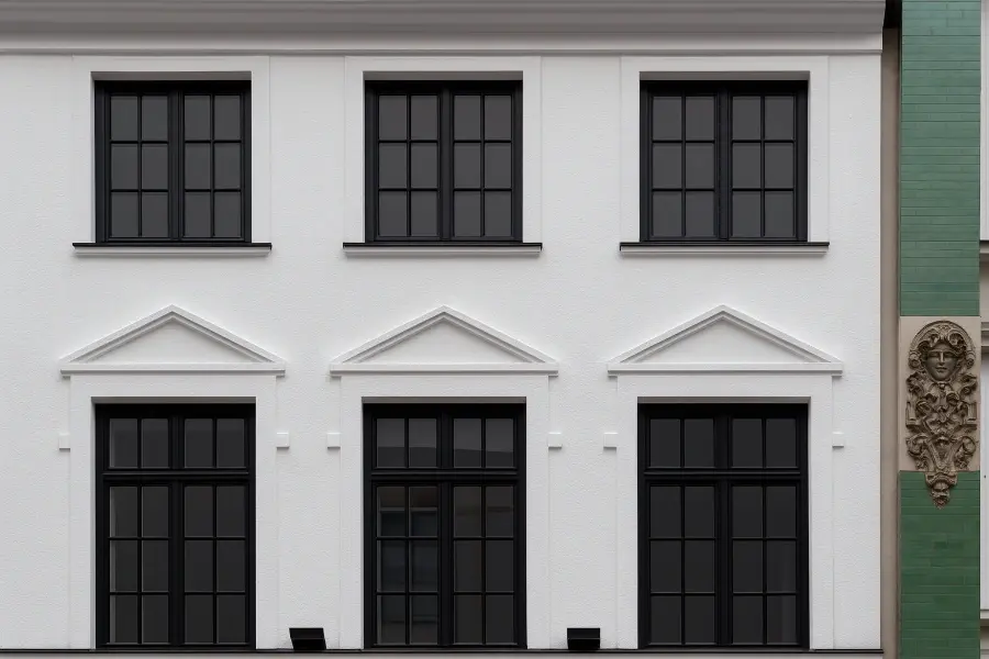 Fassadensanierung in der Stadt: weiße Putzfassade, schwarze Sprossenfenster, Gesimse und Fensterverdachungen – klassisch & gepflegt.