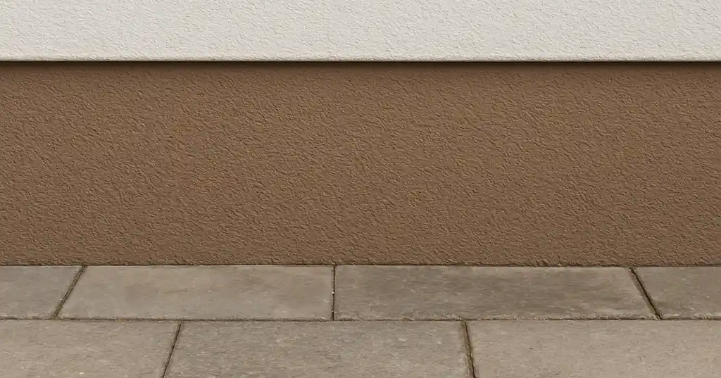 Helle Fassade mit braun abgesetztem Sockel über Pflaster