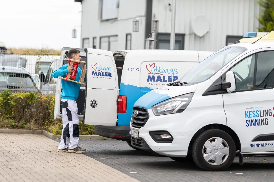 Einsatzvorbereitung: Maler lädt Leiter aus Servicefahrzeug, zweites Firmenauto daneben – startklar für Maler- und Fassadenarbeiten.