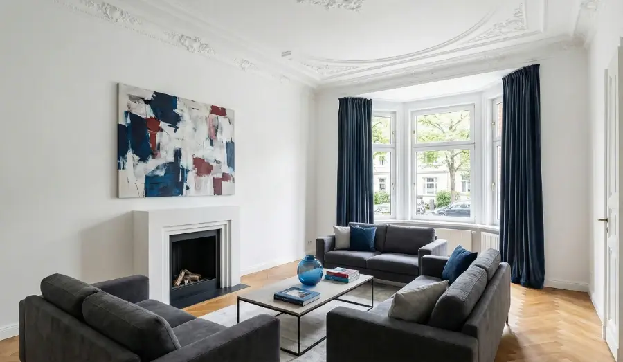 Frisch saniertes Altbau-Wohnzimmer in Hamburg mit prächtigem Stuck und modernem Interieur. Helle, glatte Wände treffen auf stilvolle Akzente in Blau und Anthrazit – meisterhafte Wandgestaltung und Bodenarbeiten.