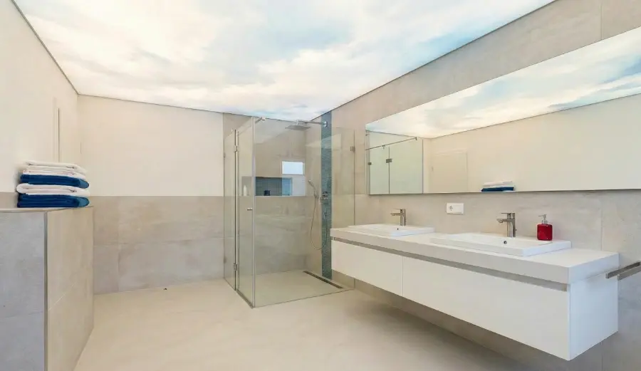 Modernes Badezimmer in hellen Tönen mit beleuchteter Spanndecke und Motiv über einem Waschtisch mit heller Platte – exklusive Badgestaltung von K und S Farbkonzepte für Hamburg und Stade.